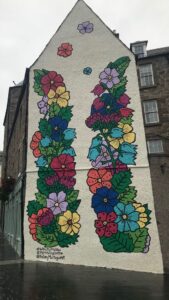 Painted mural on the side of a tall white building of brightly coloured flowers. (#WhatLiftsYouUp Kaley Montague CPK)
