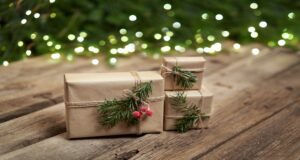 Three small presents wrapped with brown paper, string, and sprigs of fir. The presents sit on a rough wooden surface.