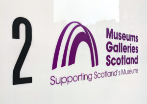 The MGS logo printed onto a white plastic background. The logo features a purple arch and the words “Museums Galleries Scotland: Supporting Scotland’s Museums”.