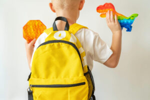 Child with yellow school bag and Sensory Fidget Toy on white background.