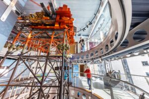 Visitors stand on two floors of balconies overlooking a multi-storey model of a bright orange oil rig.