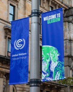 A metal post displaying two deep blue banners. One banner has the words 'United Nations Climate Change', while the other has the words ' Welcome to Glasgow' and an abstract green and white pattern.