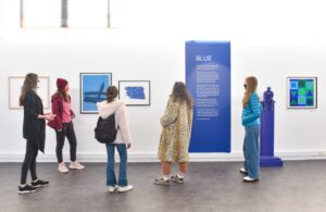 A group of adults wearing face masks look at art in the University of Stirling gallery. The artworks are all in various shades of blue.
