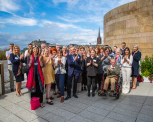 Group of programme participants smiling at the camera. Edinburgh castle and blue skyline are in the background