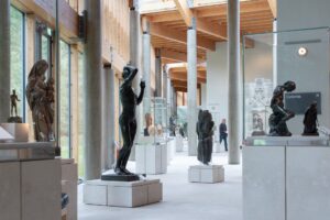 A spacious gallery at the Burrell Collection which is filled with large variety of sculptures that depict the human form. The sculptures are made of bronze, stone, and wood.