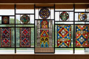 A display of brightly-coloured stained glass which features detailed floral designs, heraldry, and Christian iconography. The stained glass is on display at the Burrell Collection.