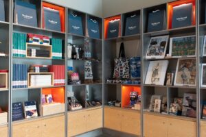 A wide range of merchandise on sale in the Burrell Collection shop. Books, prints, bags and magnets are displayed together on shelves.