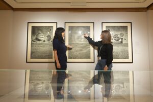 Two adults with light skin observe ‘Gravity’, a print by Nigerian-born artist Ade Adesina, at Edinburgh’s City Art Centre.