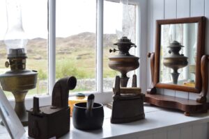 Old oil lamps and a mirror on display in a window at the Colonsay and Oransay Heritage Trust.