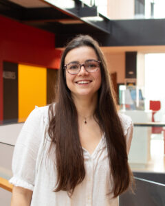 An adult with light skin, long straight brown hair, glasses, and a white blouse.