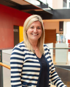An adult with light skin, long straight blond hair, and a blue and white striped cardigan.