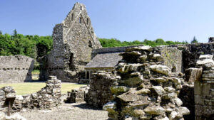 The ruins of a medieval building with thick stone walls. Behind the ruins is a forest.