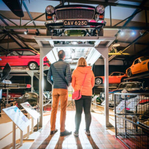 Two adults stand and look up at a display of vintage cars.