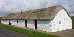 A long, low building with a thatched roof, red doors and stone walls which are painted white.