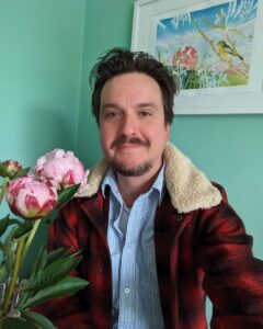 An adult with light skin, short brown hair, and a red and black plaid jacket.