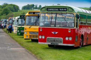 A row of colourful vintage buses parked on grass at the Scottish Vintage Bus Museum.