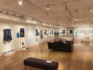 Knitted textiles are displayed in a white gallery space at Shetland Amenity Trust. Comfortable sofas are placed in the middle of the room.