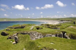 A network of low stone walls covered in turf. Behind the walls is a small bay with a long sandy beach.