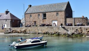The Old Tolbooth Museum in Stonehaven. It is a traditional stone building by the waterfront. Two small boats are moored in the water.