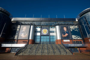 A football stadium with large banners which feature adults posing in football kits.