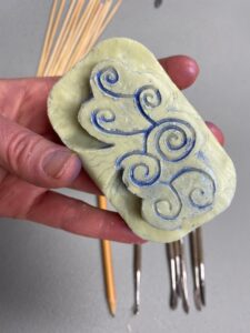 A hand with a light skin tone holds a bar of soap carved with a swirling pattern.