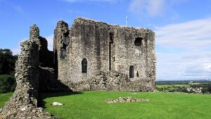 The ruins of a medieval castle. Thick stone walls and a two-storey keep are surrounded by grass.