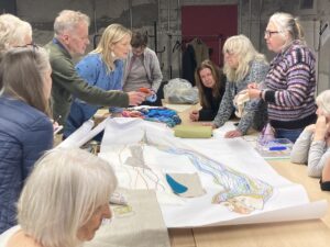 A group of people stand around a table which has a large drawing in the middle of it.