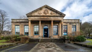 The exterior of a 19th century sandstone building with an entrance between four stone columns that hold up a pediment roof. The words "The Smith Institute" are carved above the columns.