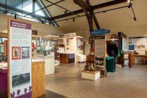 A large gallery space with a high, angled ceiling and cream walls. It contains glass cases, tall display panels, and a wide variety of objects relating to the history of Dalkeith.