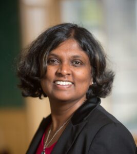 An adult with medium-dark skin, wavy dark brown medium-length hair, and a black blazer.