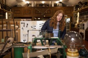 An adult with light skin and long, wavy red hair looks at a display of industrial equipment. Behind the adult are displays of agricultural equipment.