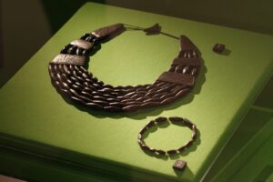 A necklace and bracelet made of black cylindrical beads, displayed on bright green fabric.
