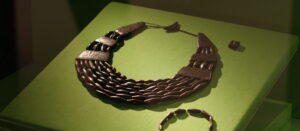 A necklace and bracelet made of black cylindrical beads, displayed on bright green fabric.