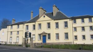 A long three-storey building with pale yellow walls, a large blue door, and a grey tiled roof.