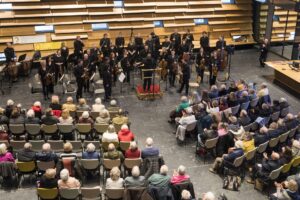 An orchestra stands for applause in front of rows of seated people.