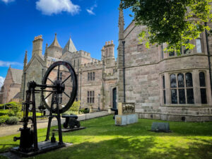 An ornately decorated two-storey building made of light grey stone. Art works, small cannons, and an early industrial machine are displayed on the lawn in front of the building.
