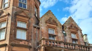 The upper floors of a building made of red stone. The building has ornate pediments and balconies.