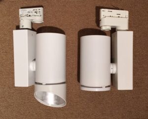 Two similar looking white cylindric lights with white adaptor fittings. The lefthand light has a white snoot attached to it.