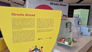 A yellow information board about an exhibition called Streets Ahead. The exhibition is an design challenge which actively involves young people to reimagine the high street.