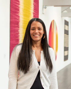 A smiling adult with medium-tone skin, long straight black hair, and a white cardigan.