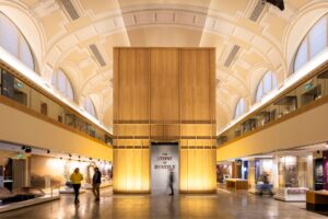 A large gallery with a curved ceiling and wide first-floor balcony. A two-storey wooden structure stands in the middle of the gallery. The structure has an entrance displaying the text "The Stone of Destiny".
