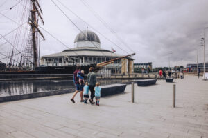 Two adults and three children on a walkway in front of a large black sail ship with the text "Discovery" on its side.