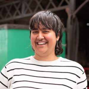 An adult with a medium skin tone, dark-brown shoulder length hair, and a white t-shirt with black horizontal stripes.