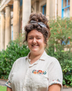 An adult with light skin, long brown wavy hair tied into an updo, and a white shirt.