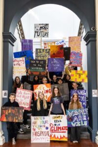 A group of children standing on a staircase and holding hand-painted placards which feature messages about political and social issues.
