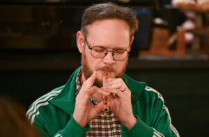 An adult with light skin tone and short dark hair. They are playing a wooden flute.