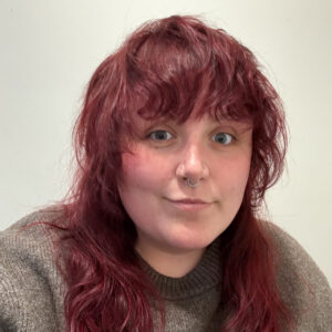 An adult with light skin and wavy, long, deep red hair.