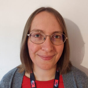 An adult with light skin, straight shoulder-length light brown hair, and glasses.