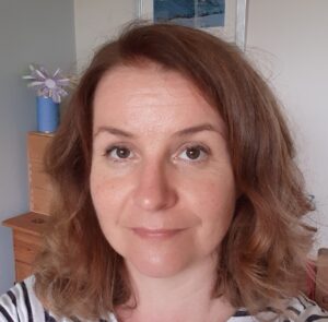 An adult with light skin and wavy brown shoulder-length hair.