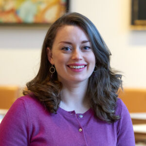 An adult with light skin, long wavy brown hair, and a purple cardigan.